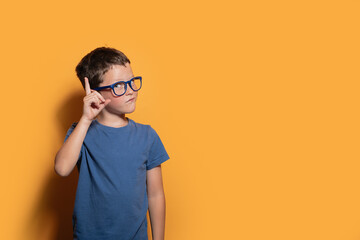 Thoughtful boy with glasses on yellow background