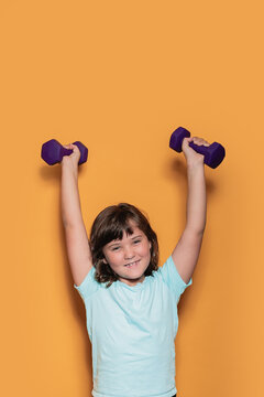 Cheerful child lifting weights on orange background