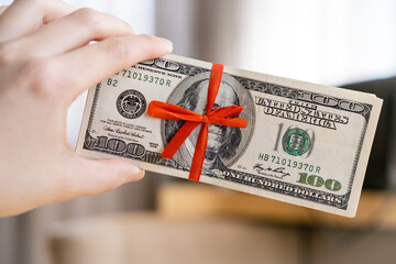 Bundle of dollars is wrapped in a thin red ribbon folded into a bow