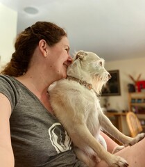 Woman kissing dog on lap at home