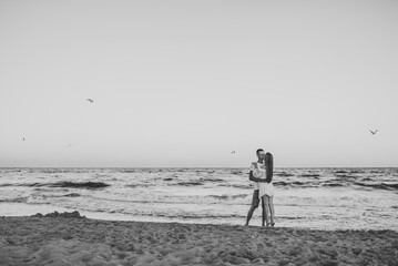Man embraces woman walks on sand sea. Couple in love hugging and kissing on seashore. Female kisses...
