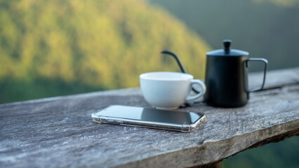 mobile smartphone left on wood table with blurred coffee cup kettle and blurred moutain view...