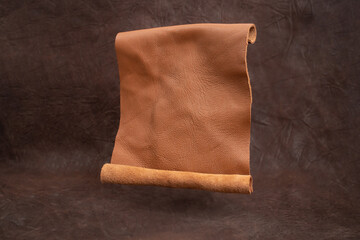 Opened genuine leather scroll levitating on brown vignette  background, abstract textured backdrop