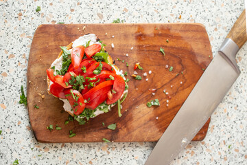 Toast slice of bread with spread cheese, chopped tomato and spring onions on a wooden chopping...