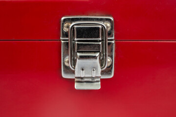 Stainless steel snap lock on a red metallic case, closed lid of a red painted box, soft focus close...