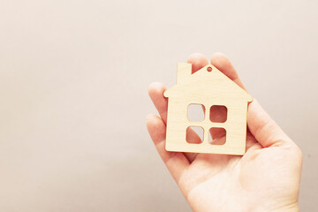Human hand holding a wooden toy house on a beige background. Buying a house or family psychology