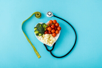 organic vegetables on heart-shape plate near measuring tape and stethoscope on blue