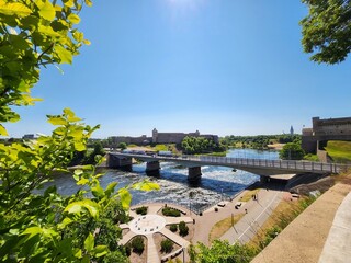 The river flows through the city with a bridge in the distance. The sky is clear and blue with a...