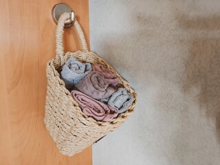 A close-up view of a beautifully crafted woven straw basket hanging on a rustic hook, filled with towels in shades of green, pink and gray, adding charm and practical organization to the space. - Powered by Adobe