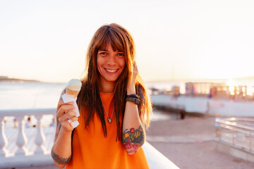 Portrait of young pretty happy Caucasian woman with tattoos holds ice cream at sunny beach. Concept...
