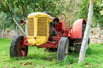 A old red rusty tractor in the garden with trees.