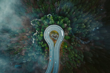 Aerial view of a beautiful round road surrounded by autumn forest during a foggy morning in the...