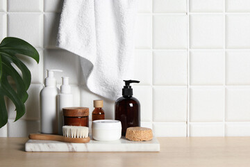 Different bath accessories and personal care products on wooden table near white tiled wall, space...