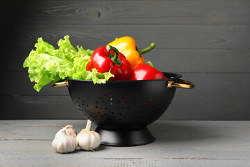 Black colander and different vegetables on rustic wooden table