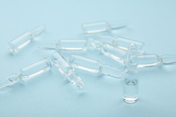 Glass ampoules with liquid on light blue background, closeup