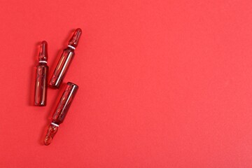 Glass ampoules with liquid on red background, top view. Space for text