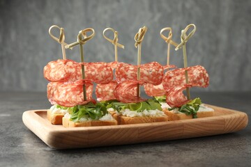 Tasty canapes with salami, greens and cream cheese on grey table