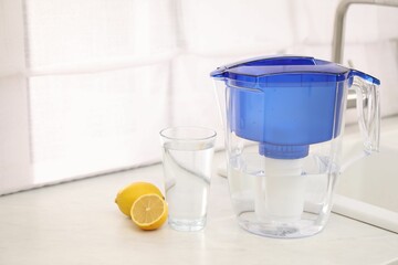 Water filter jug, glass and lemons on countertop in kitchen, space for text