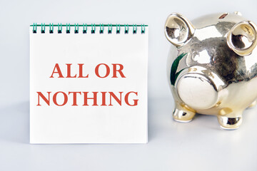All or nothing, motivational phrase on a vertically standing notebook near the piggy bank on a light background