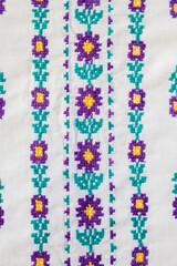 cross stitch floral motifs in purple yellow and green shades on white cotton fabric. Embroidery on traditional Slavic clothing.