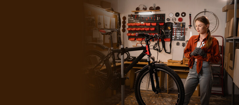 Bike service, repair and upgrade concept. Cycling mechanic checking bicycle, holding wrench while fixing bicycle in workshop. Young female servicewomen.