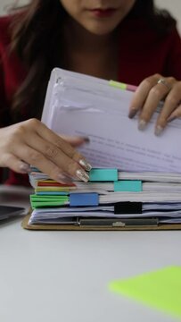 A woman doing paperwork is searching for a sheet of paper in a pile of documents on her desk.