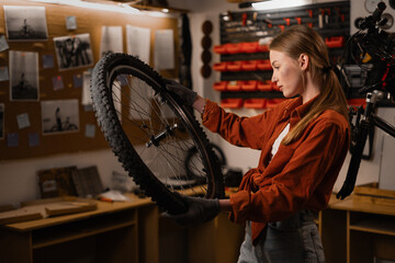 Young woman bicycle mechanic fixing cycle wheel in repair shop. Bike shop engineer fix bicycle...
