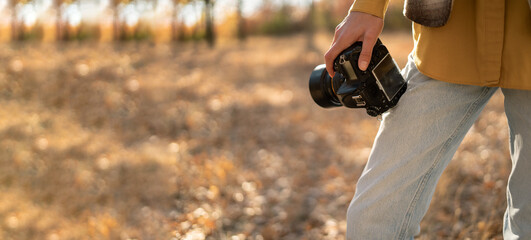 Close-up of female photographer holding a camera in front of a path in a forest, nature travel and...