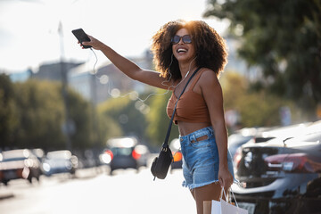 Smiling woman raising hand calling taxi standing on road in city