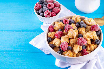 Tiny breakfast croissants cereals with fresh berries and milk. Bowl portions with trendy fresh baked mini petite croissants with raspberry and blueberry, dessert morning snack