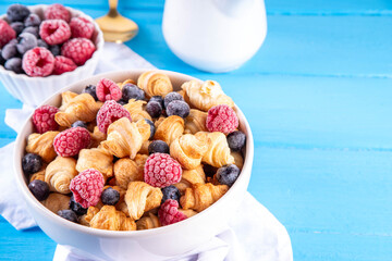 Tiny breakfast croissants cereals with fresh berries and milk. Bowl portions with trendy fresh...