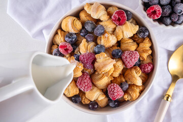 Tiny breakfast croissants cereals with fresh berries and milk. Bowl portions with trendy fresh baked mini petite croissants with raspberry and blueberry, dessert morning snack