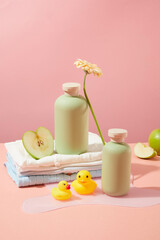 Bathroom layout with many products and toys for baby, Empty label bottle for advertising product made from organic ingredients over light pink background. Front view, copy space