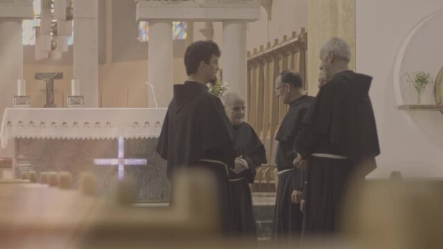 Christian monks wearing brown robes standing in church and talking medium shot. Elderly and mid adult caucasian clergymen group chatting in cathedral