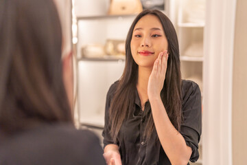Smiling of beautiful asian woman fresh healthy white skin, clean, looking at mirror.asian girl touching on face applying cream, skincare, cosmetics, cosmetology, beauty, fashion at home.spa, wellness