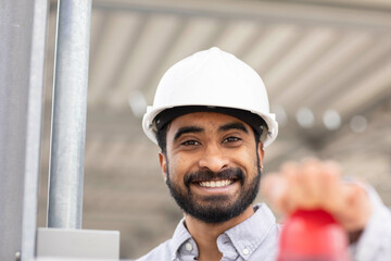 A smiling man with a beard wearing a white hard hat pressing the red button