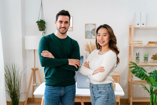 Confident man and woman posing with arms crossed in a modern office.