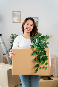 Woman smiling and holding a moving box with a plant