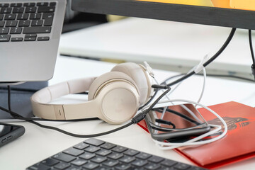A pair of white headphones is resting on a red notebook beside a laptop on a desk.