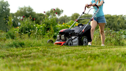 girl with a lawn mower mows the lawn in front of the house