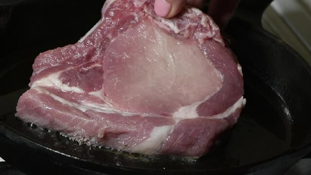  Place a raw pork cutlet on the bone in a preheated frying pan. Close-up