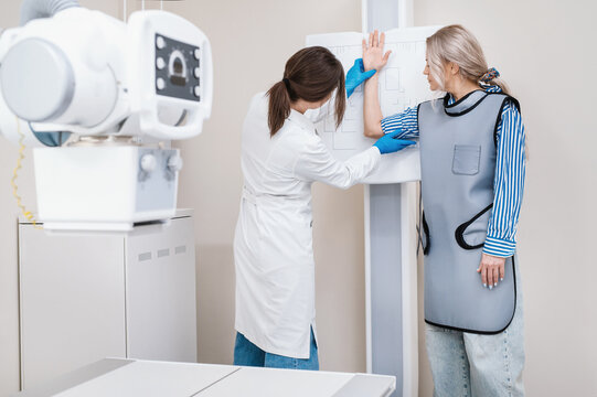 Female doctor takes a photo of a woman patient’s hand against the background of a special target to make an x-ray in an office with an x-ray machine, medical equipment.
