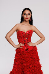 Fototapeta premium A beautiful brunette with long hair is dressed in Russian folk style, a long red dress with a corset and kokoshnik. Beautiful smile, lips with red lipstick, white background. A pretty slender girl 