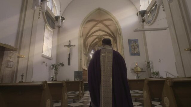 Priest in purple robe walking through church aisle to sanctuary back view tracking shot. Religious liturgy, sacred worship and mass ceremony concept