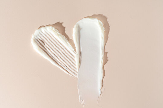 Heart-shaped white cream smears on beige background