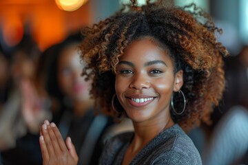 A mid-shot of an attractive woman with curly hair clapping hands and smiling in a social event setting