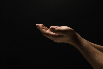 Religion. Man with open palms praying on black background, closeup. Space for text - obrazy, fototapety, plakaty