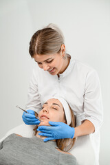 Specialist makes a beauty procedure on a face of a woman in a gray sweater on a white background