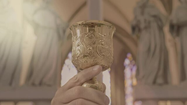 Christian priest raising sacramental wine golden chalice close up. Clergyman in purple robe lifting goblet near christian church altar. Eucharist ceremony symbol