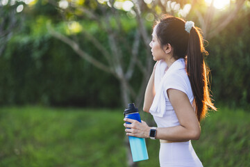 Attractive young Asian woman who is thirsty is drinking water while taking a break from jogging at...